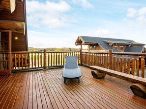 A wooden deck with a wicker chair, wooden railings, and a view of a building and landscape. - 5 Star Holiday Home in Nimtofte (Nimtofte)