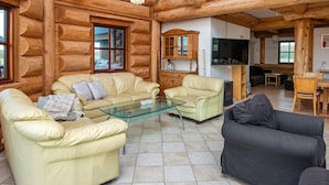 Interior de cabana de tronco com sala de estar, apresentando dois sofás, uma mesa de centro de vidro e uma televisão.