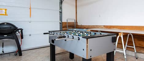 A room with a foosball table, a chair, and a ladder.