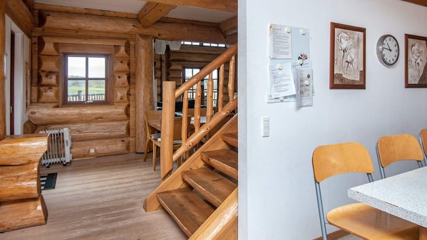 Interior de uma cabana de madeira com escada, área de jantar e vista pela janela.