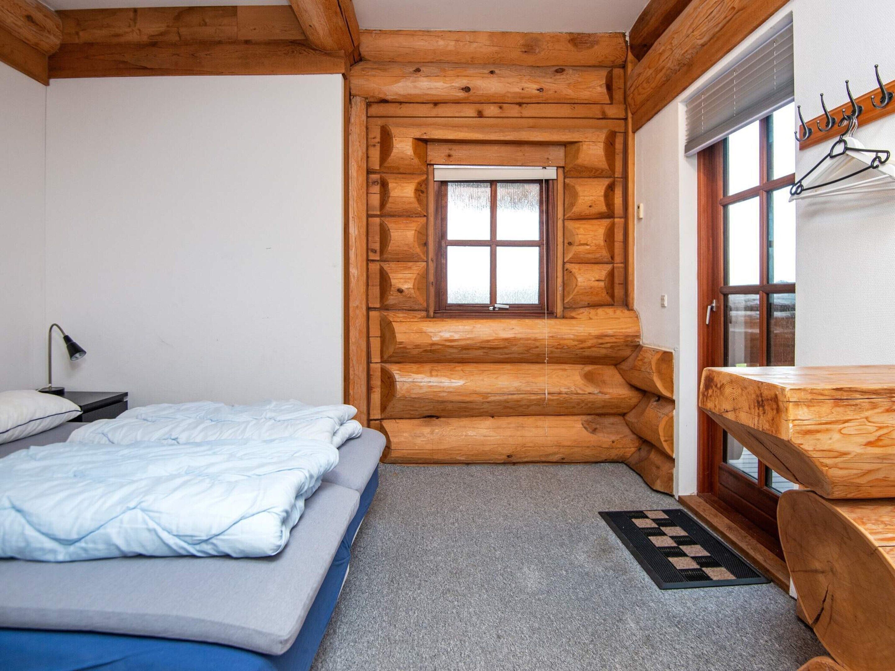 A log cabin bedroom with a bed, a desk, and a window.