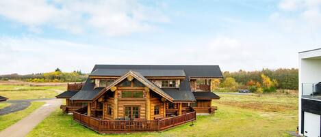 A log cabin with a porch, a garage, and a large open grassy area.