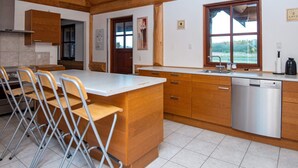 Cozinha moderna com vigas de madeira, ilha central, máquina de lavar louça e vista pela janela.