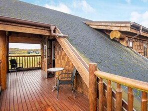 A wooden deck with a table and chairs, a view of the landscape, and a building with a sloped roof. - 5 Star Holiday Home in Nimtofte (Nimtofte)