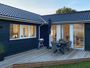 A modern house with a dark exterior, a wooden deck, a barbecue grill, and a dining area with chairs and a table. - 4 Star Holiday Home in Hadsund (Hadsund)