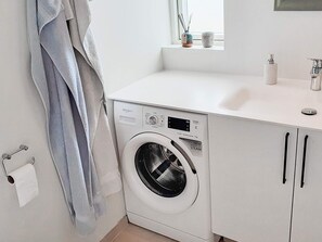 A compact, modern laundry room with a front-loading washer and dryer, a white sink, and a window above the counter. - 4 Star Holiday Home in Hadsund (Hadsund)