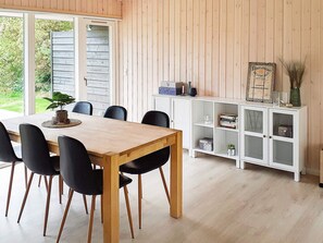 Ein Essbereich mit einem Holztisch und Stühlen, einem weißen Schrank mit Glastüren sowie Blick ins Grüne.