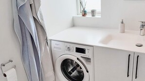 Un lavadero pequeño y moderno con lavadora y secadora de carga frontal, una encimera blanca y una ventana sobre el lavabo.
