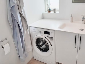 A compact, modern laundry room with a front-loading washer and dryer, a white countertop, and a small window above the sink.
