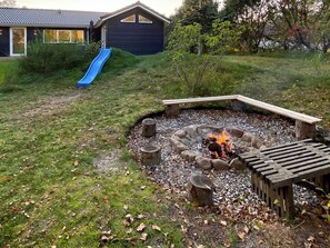 A backyard with a fire pit, a wooden deck, and a blue slide. - 4 Star Holiday Home in Hadsund (Hadsund)