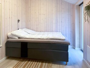 Ein Einzelbett mit einer Matratze und einem dunklen Gestell, platziert vor einer Wand mit vertikalen Holzpaneelen.