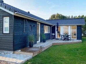 A modern house with a dark exterior, a wooden deck, a barbecue area, and a glass door leading to a patio. - 4 Star Holiday Home in Hadsund (Hadsund)