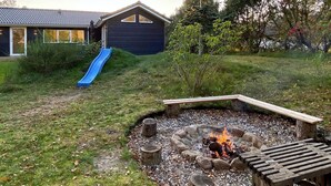 Un patio trasero con un pozo de fuego, una terraza de madera y un tobogán azul.