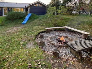 A backyard with a fire pit, a wooden deck, and a blue slide.