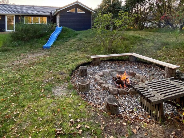 A backyard with a fire pit, a wooden deck, and a blue slide.