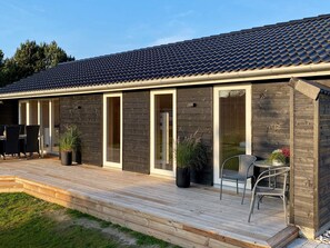 En moderne bygning med et tegltag, en træterrasse og et overdækket udendørs siddeområde.