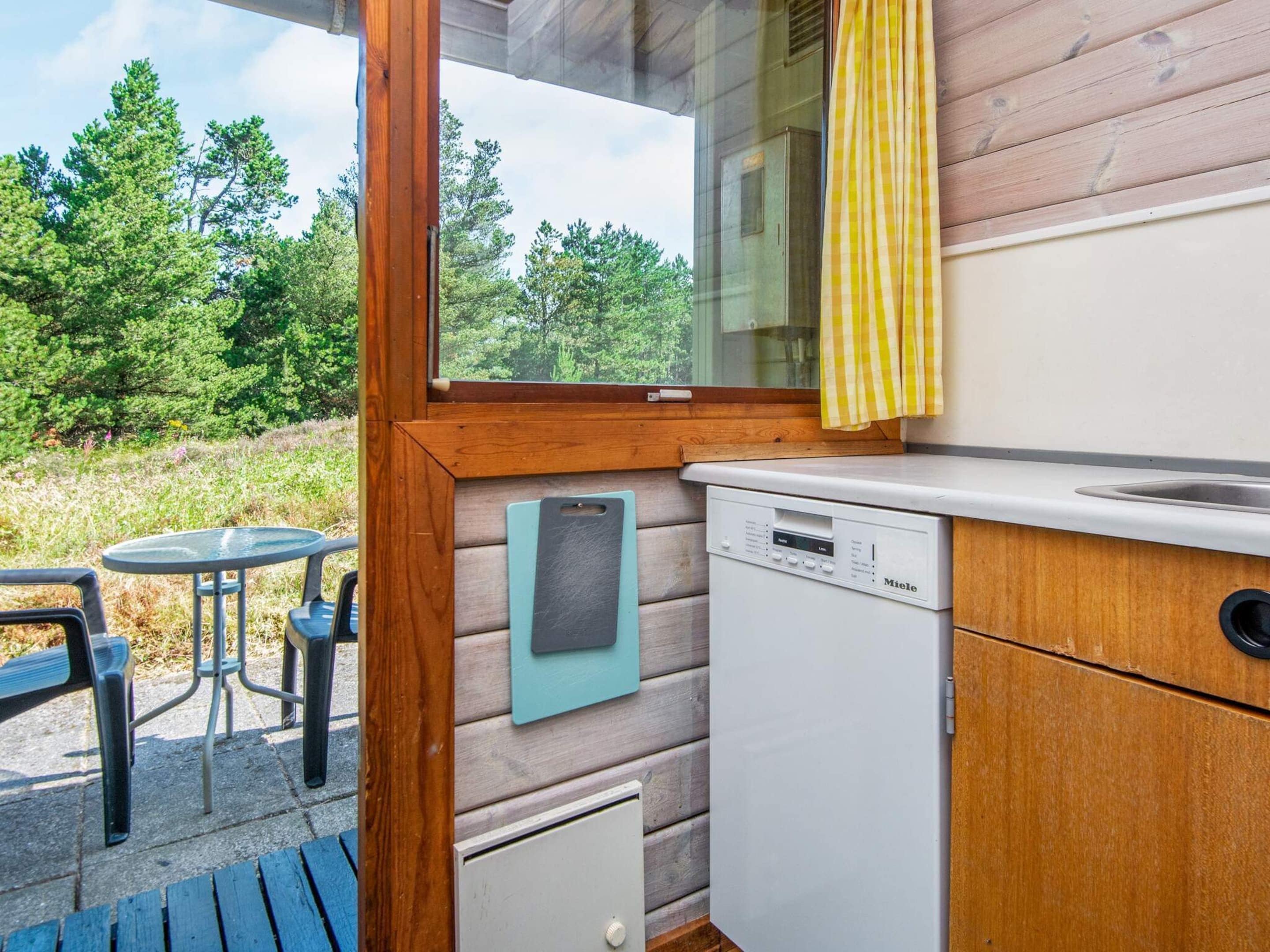 Une cuisine compacte dotée d’un lave-vaisselle intégré, d’une petite table et d’une fenêtre donnant sur un paysage naturel.