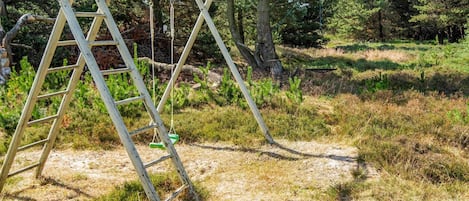 A wooden swing set in a natural setting with trees and grass.