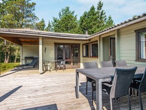 A wooden deck with outdoor furniture, a covered patio area, and a building with large windows and a chimney.