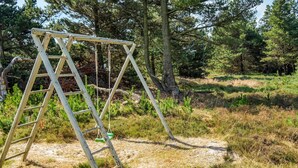 A wooden swing set in a natural setting with trees and grass.