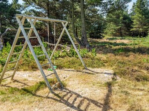 A wooden swing set in a natural setting with trees and grass.
