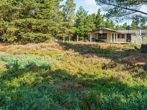 A cabin with a porch and a swing set, surrounded by dense forest and grassy terrain.