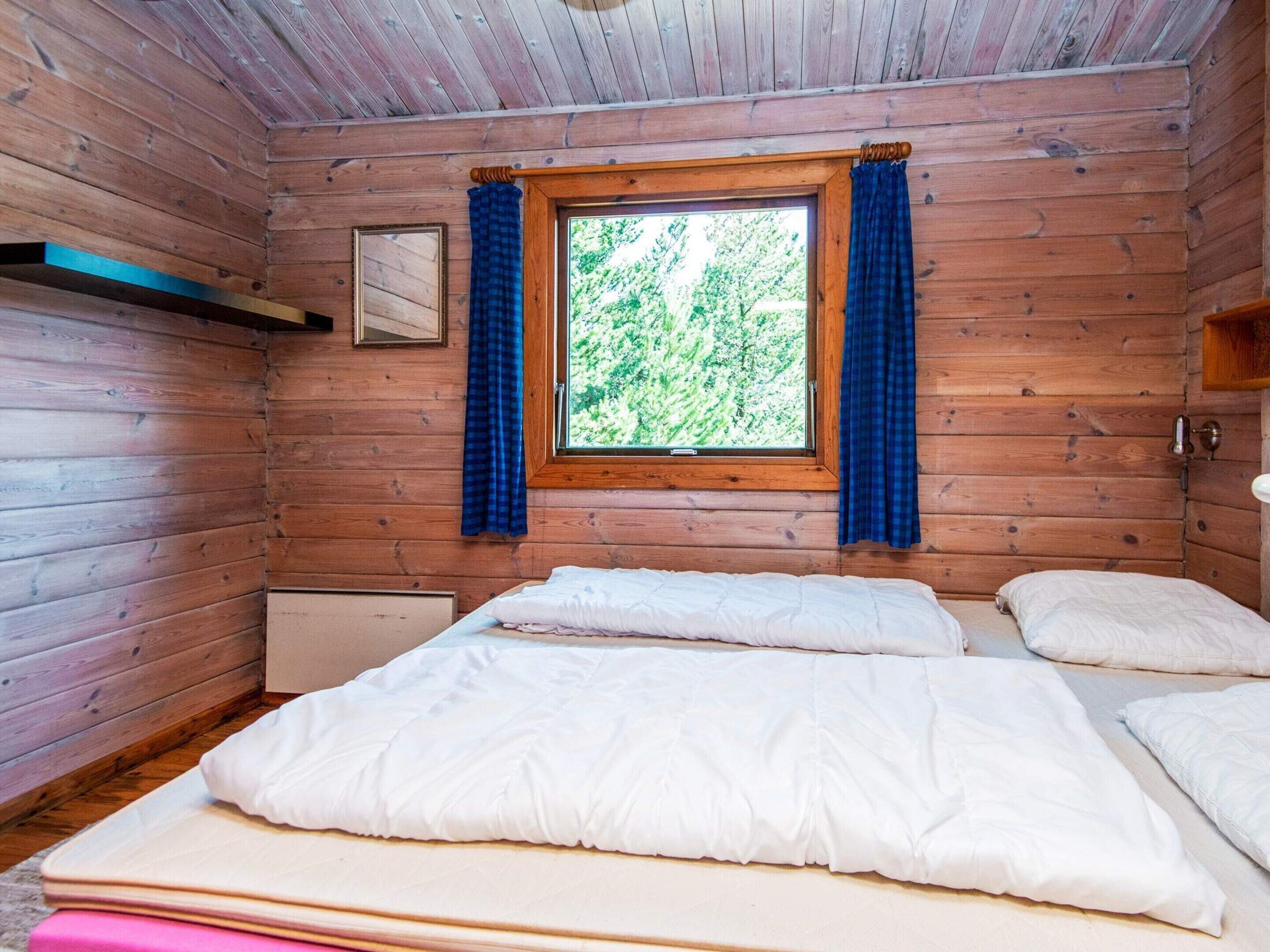 A wooden cabin room with a bed, a window with curtains, and a framed picture on the wall.
