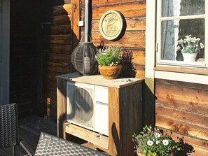 A wooden cabin with a Mitsubishi air conditioning unit on the porch, a potted plant, and a wall-mounted clock.