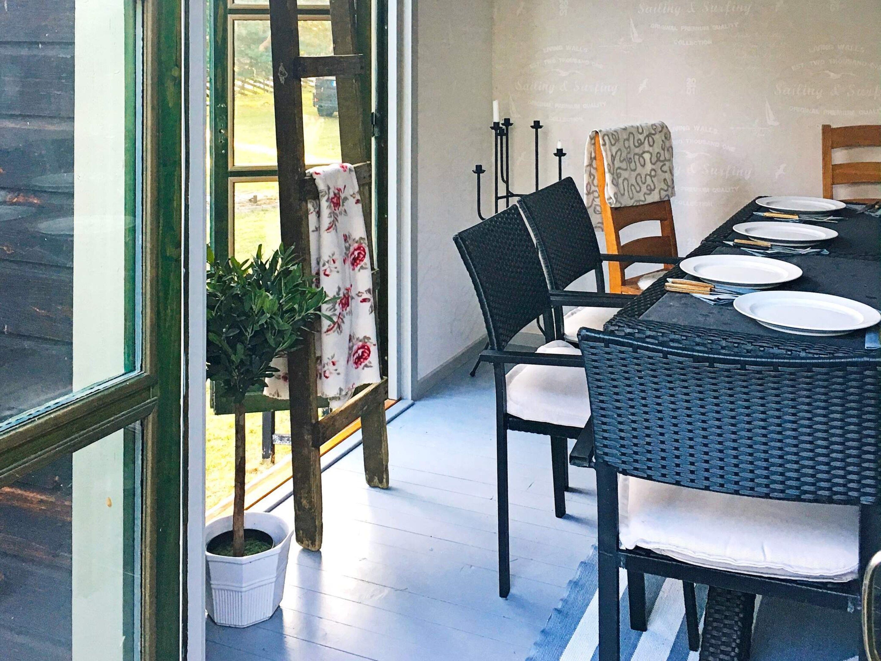 A dining area with a table set for four, surrounded by chairs, a potted plant, and a view of the outdoors.