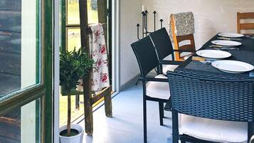 A dining area with a table set for four, surrounded by chairs, a potted plant, and a view of the outdoors.