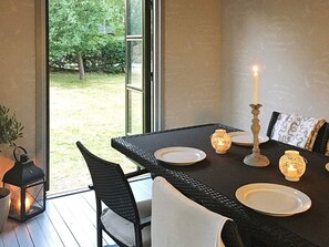 Un coin repas avec une table dressée pour deux personnes, agrémenté d’un chandelier et offrant une vue sur l’extérieur.