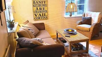 A cozy living room with a sofa, armchair, and a coffee table. There is a wall-mounted sign with text and a hanging light fixture.