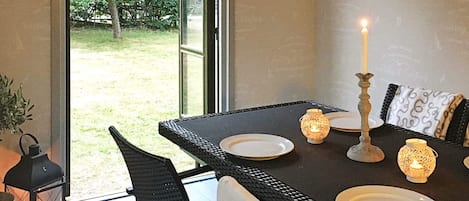 An outdoor dining area with a table set for two, featuring wicker chairs and a candle centerpiece.