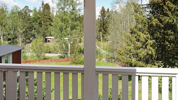 A wooden deck with a white railing overlooking a forested area with a small building in the distance.