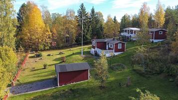 A red cabin with a white porch, surrounded by a grassy area and trees.
