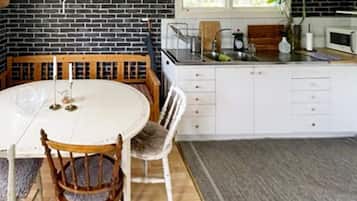 A kitchen with a round table, chairs, a white cabinet, a microwave, and a window.