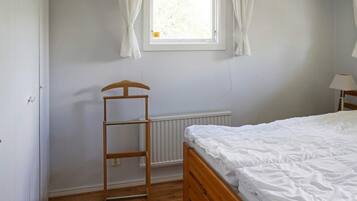 A bedroom with a wooden bed, a window with curtains, a radiator, and a wooden ladder.
