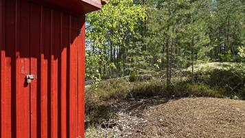 Una estructura roja de madera con una puerta de metal, rodeada por un área boscosa con árboles y matorrales.