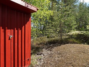 A red wooden structure with a metal door, surrounded by a forested area with trees and underbrush. - 5 Person Holiday Home in Strangnas (Strängnäs)