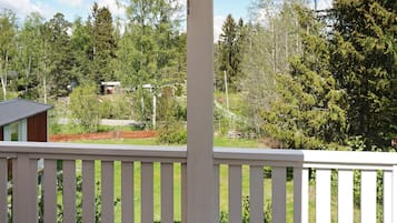 A wooden deck with a white railing, overlooking a forested area with a small building and a fenced yard.