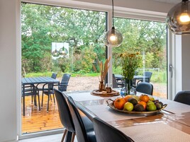 Un comedor interior con una mesa preparada para dos personas, un cuenco de fruta y un jarrón con flores.