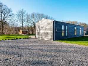 A modern building with a gravel driveway and a wooden structure in the background.