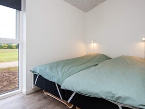 Cama de solteiro com colcha verde e estrutura preta em quarto com paredes brancas e janela.