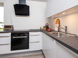 Una cocina moderna con armarios blancos, un horno negro, un lavaplatos de acero inoxidable y una tetera sobre la encimera.