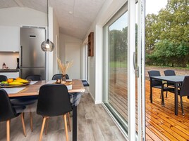 Una cocina moderna con refrigerador empotrado, un comedor con mesa de madera y sillas negras, y un puerta corrediza de vidrio que da a una terraza al aire libre.