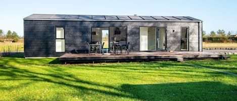 A modern, single-story house with a flat roof, large windows, and a deck area.