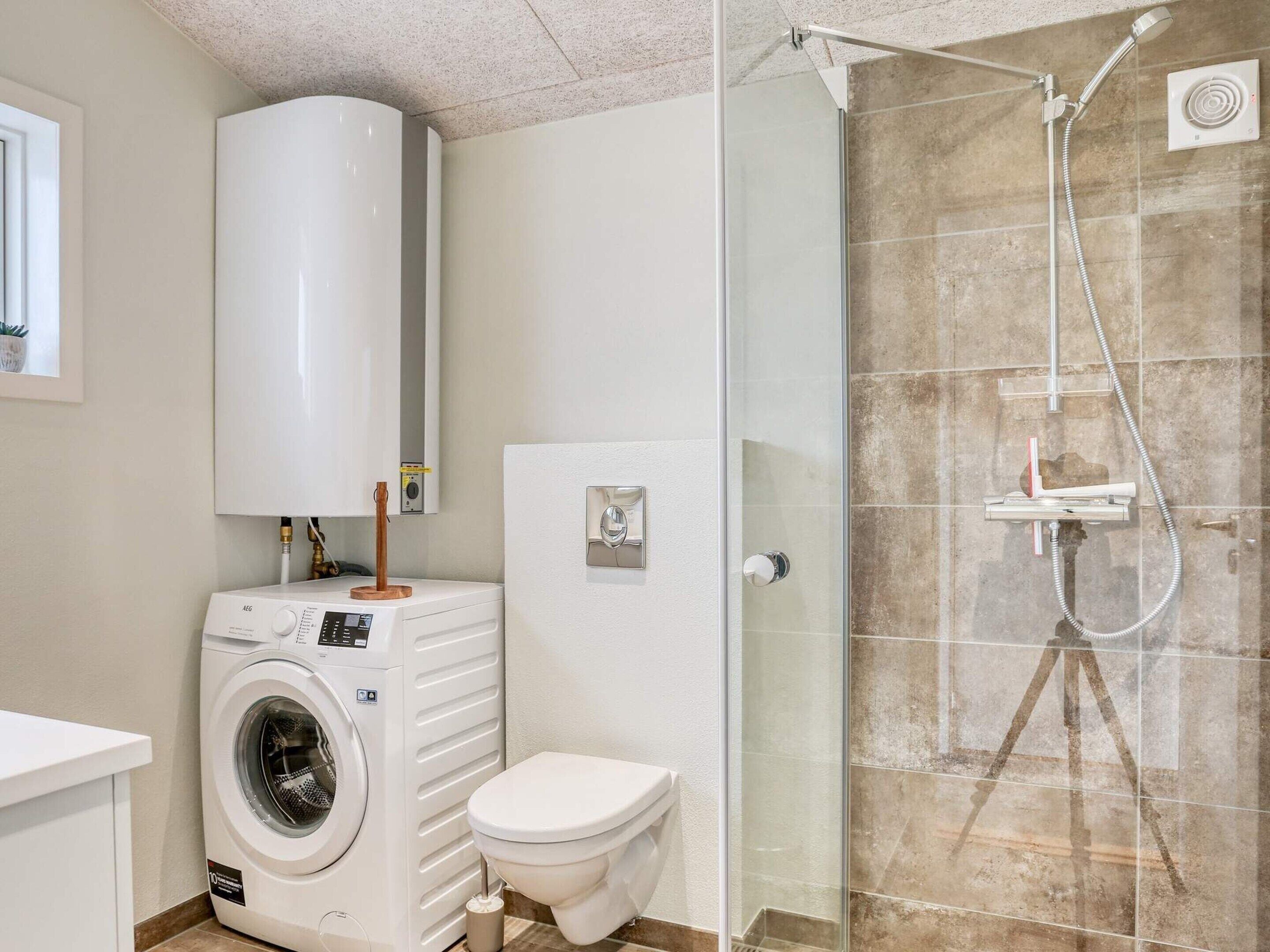 Un bagno moderno con lavatrice, WC e cabina doccia in vetro.