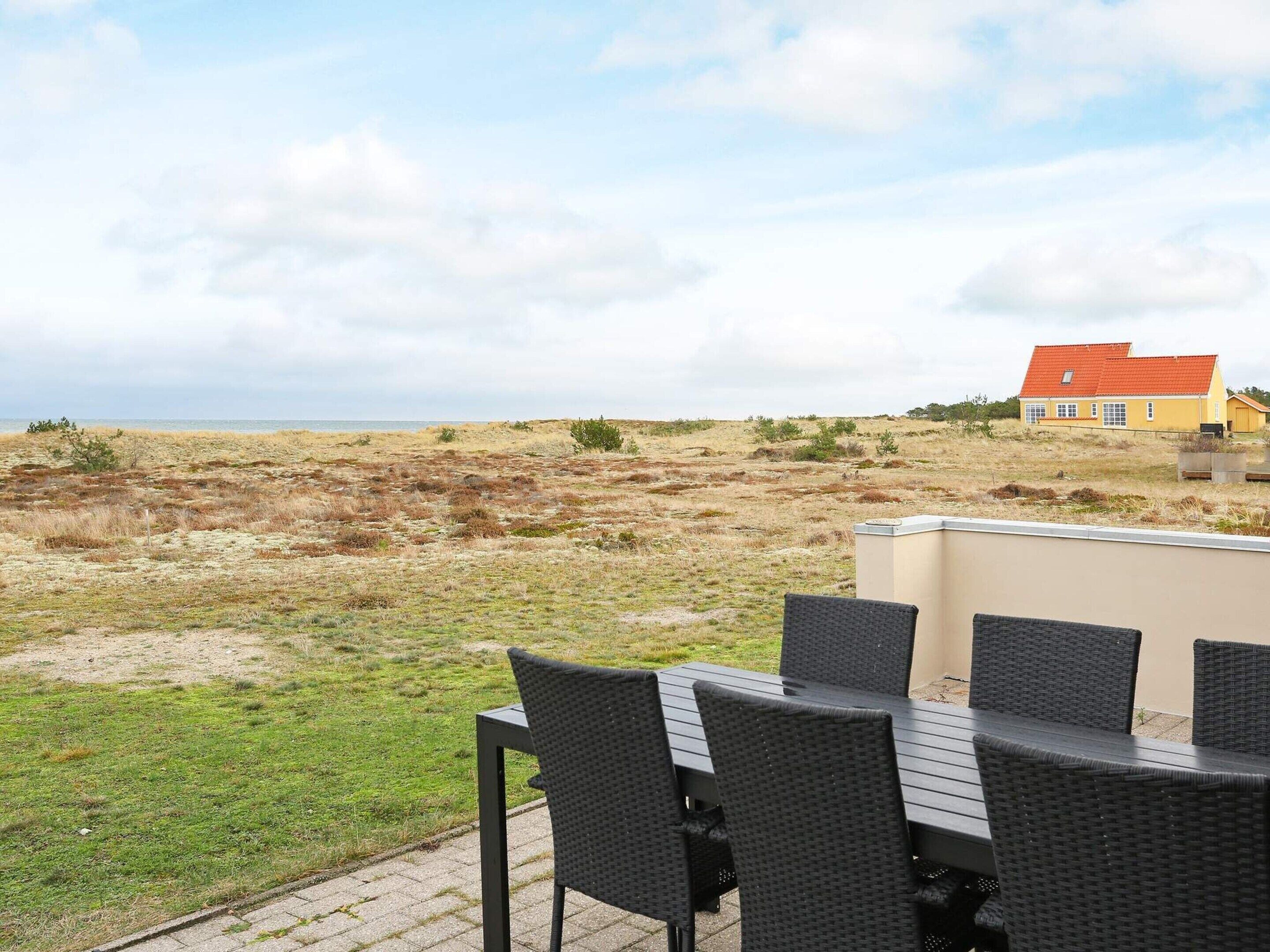 A patio with a table and chairs overlooking a beach and a yellow house.