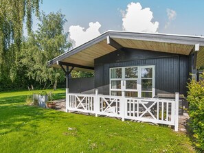 Eine Holzhütte mit Veranda, großen Fenstern und einer umzäunten Terrasse.