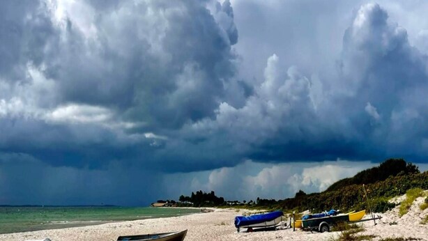 A beach with boats and a trailer, under a cloudy sky.